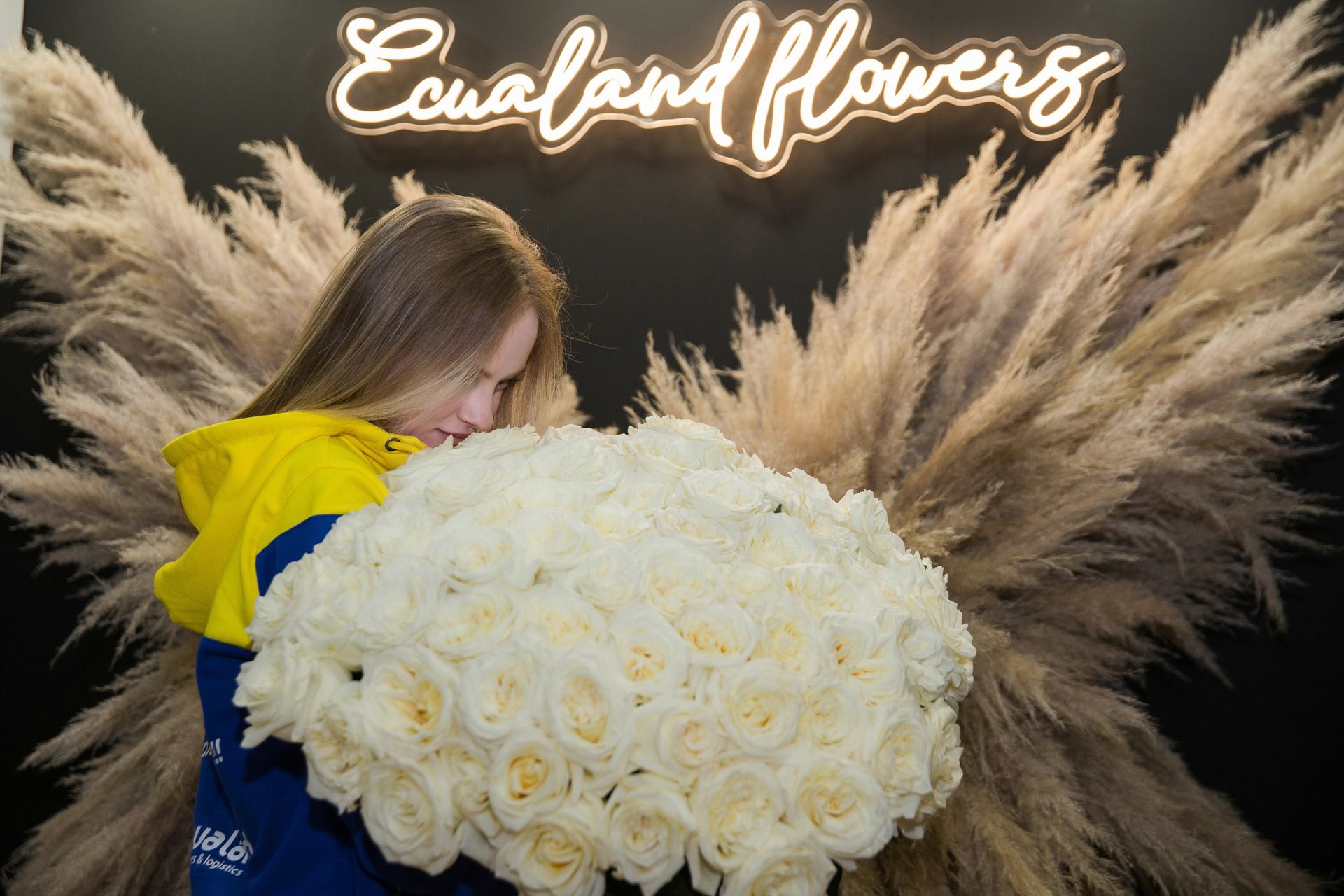 Сотрудница Ecualand с охапкой белых эквадорских роз под неоновой вывеской Ecualand flowers